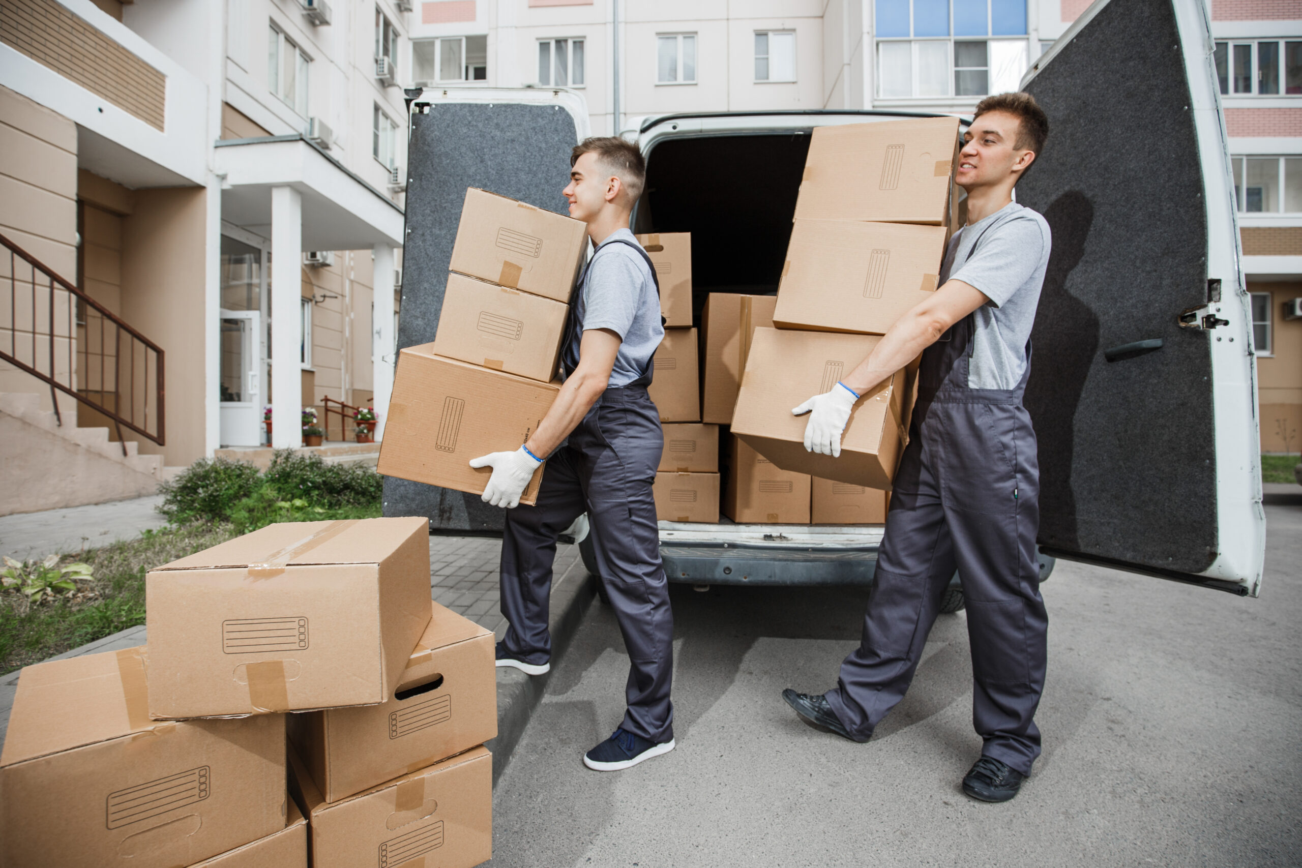 Zwei Möbelpacker tragen mehrere Kartons aus dem Transporter zur Wohnung