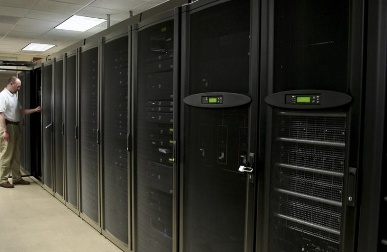 Ein IT-Mitarbeiter in einem Serverraum schaut in einen Serverschrank