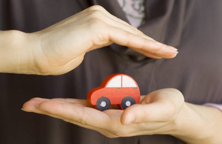 Zwei Hände beschützen ein kleinen, rotes Holzauto